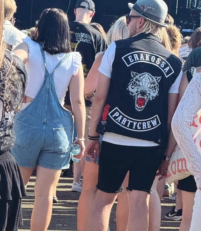 Festarikentällä keikkayleisöä, etualalla Partycrew-liivi selin kameraan.