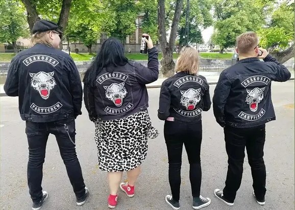 Neljä Partycrew-liiviin pukeutunutta kuuntelijaa takaa kuvattuna.
