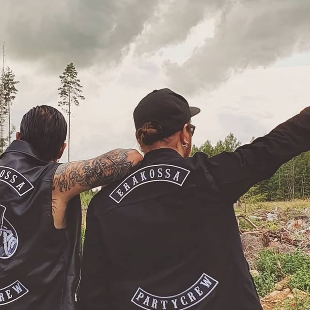Kaksi Erakossa Partycrew -liiviin pukeutunutta henkilöä selin kameraan metsämaisemassa.