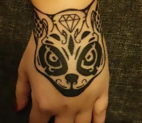 Mustalla tehty kissankasvoinen tatuointi, jonka otsalla on timantti, kädenselässä.